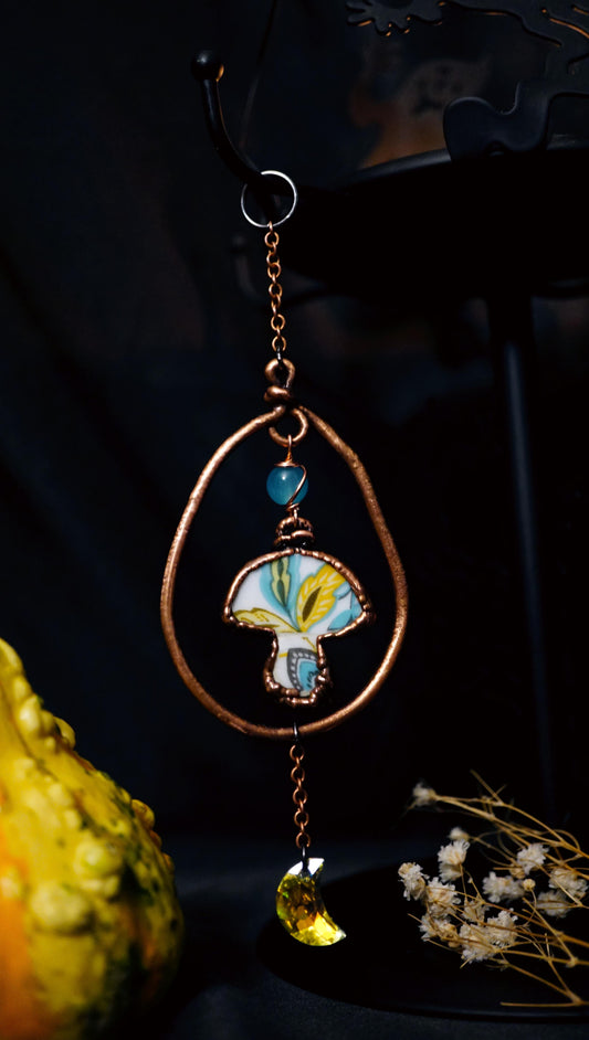 mushroom wall hanging with copper hoop and flashy crescent moon dangling below. black background