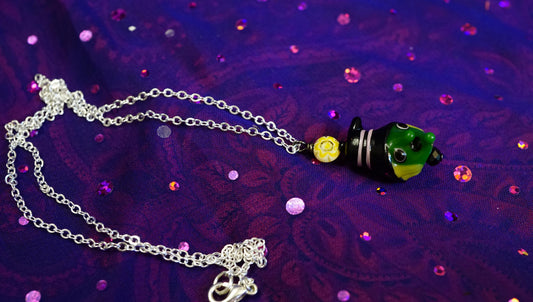 beaded necklace on purple background. green witch head bead with yellow hair and sun bead. silver chain.