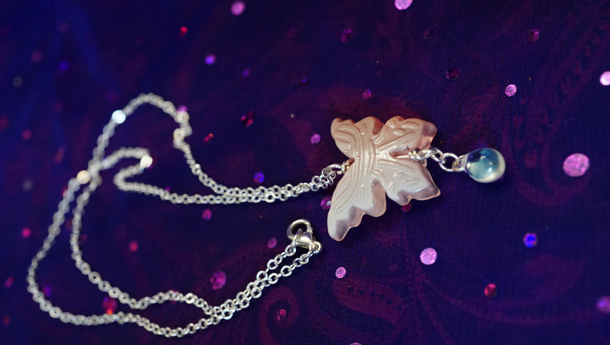 bac of a peach butterfly necklace with aura glass drop. silver chain. purple glitter background