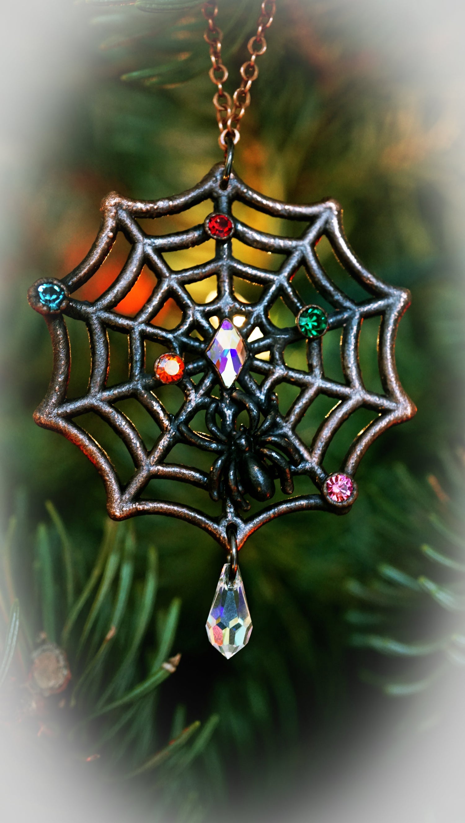 nightmare before christmas style web ornament in copper with black spider. crystal drop at bottom and "christmas light" rhinestones in many colors. hanging on green fur tree
