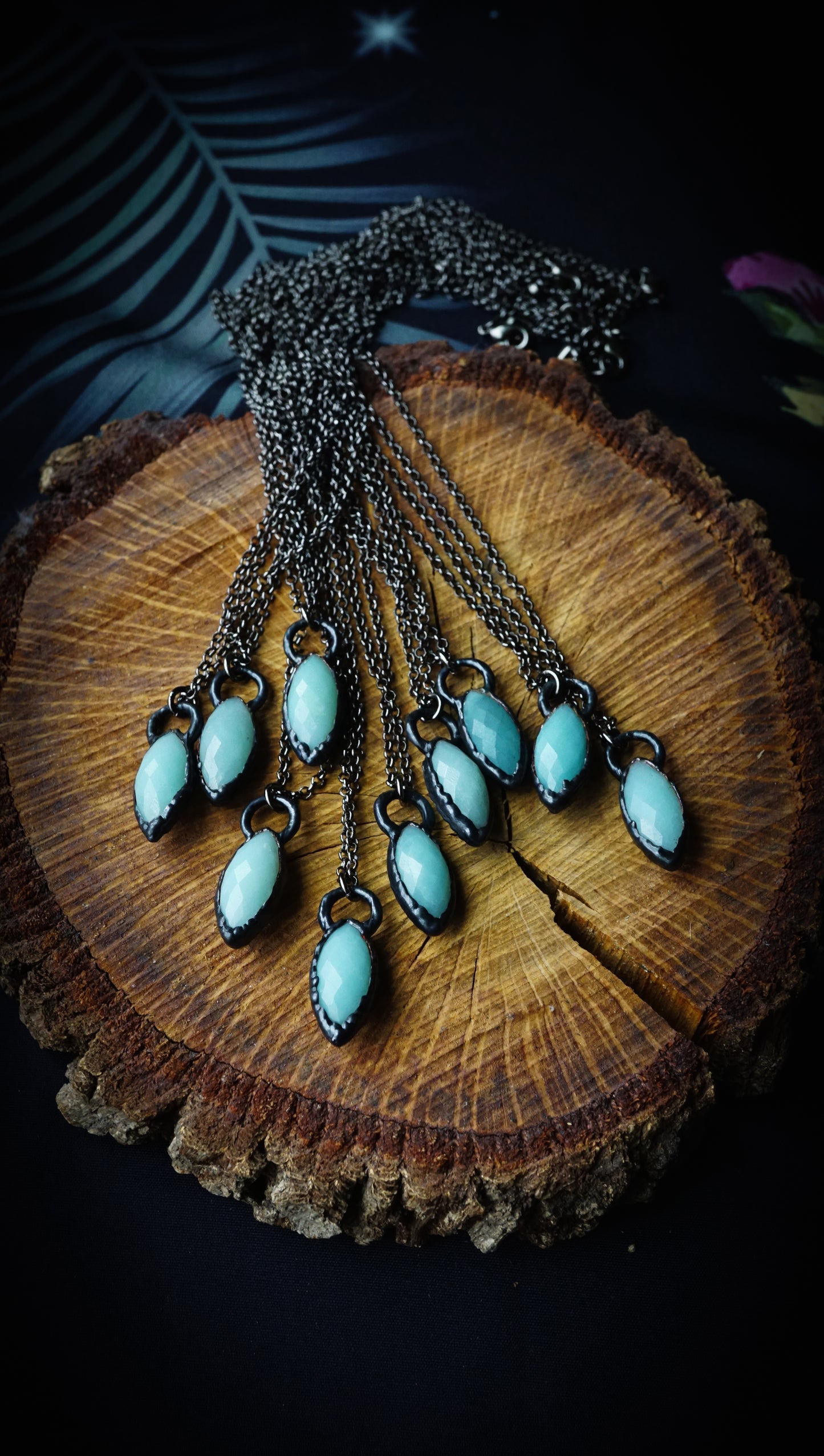 small light blue pendants with black copper and chains, on wood round against floral background