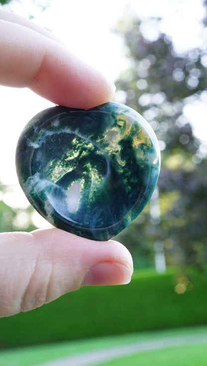 Hand holding a green and white moss agate stone up to the sun.