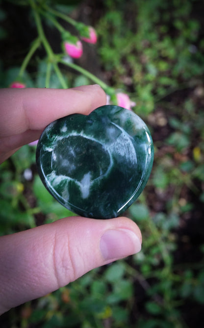 Heart-shaped green stone held between fingers with a blurred natural background