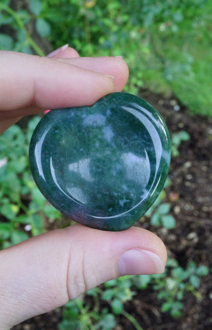 Hand holding a green stone against a natural background