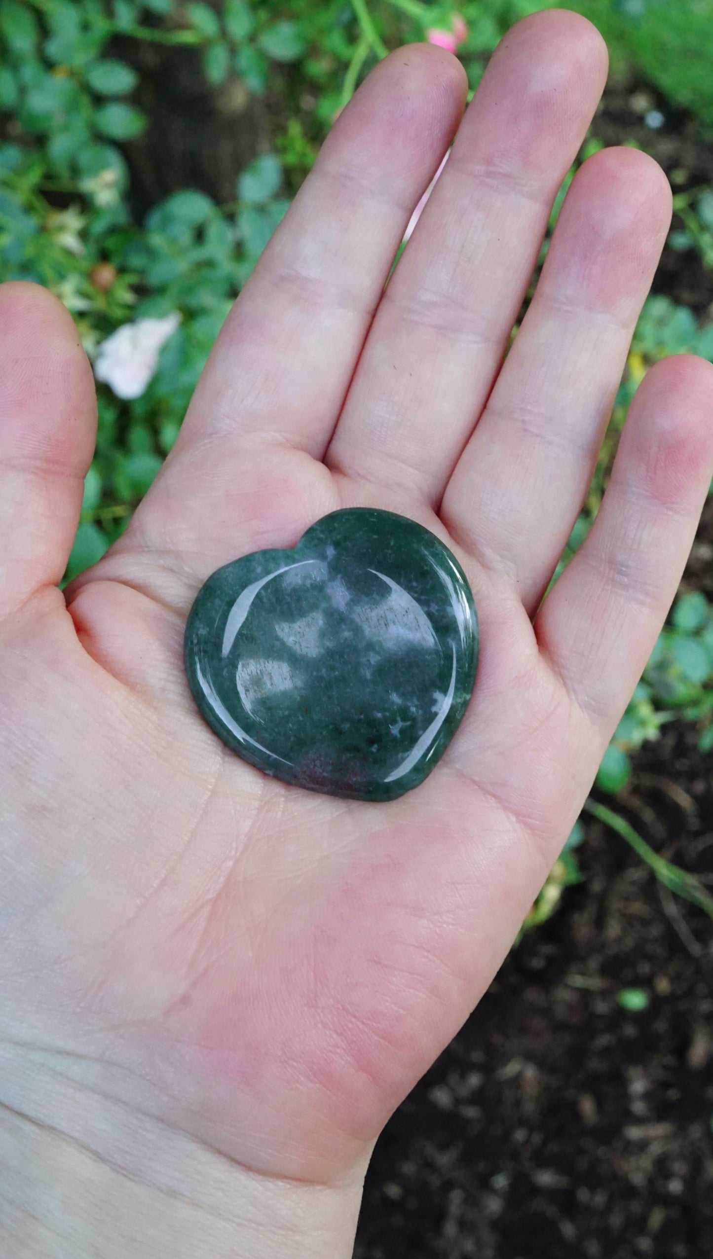 Heart-shaped green stone held in a hand with a natural background