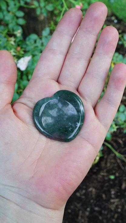 Heart-shaped green stone held in a hand with a natural background