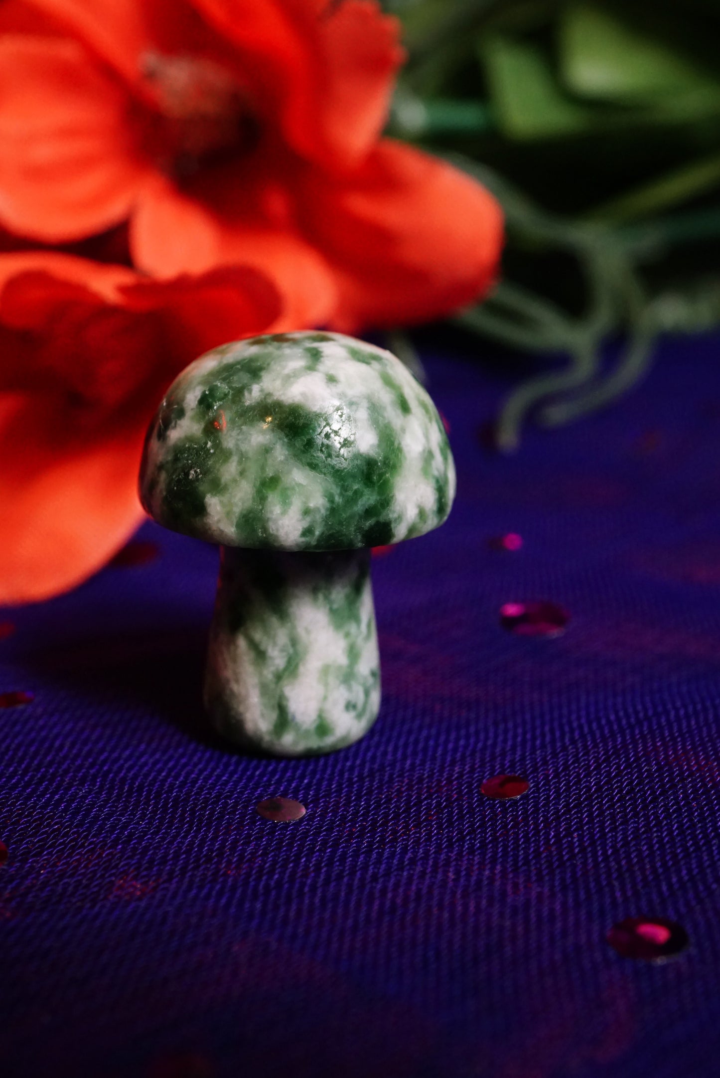 Green stone mushroom on a purple fabric background with red flowers in the background