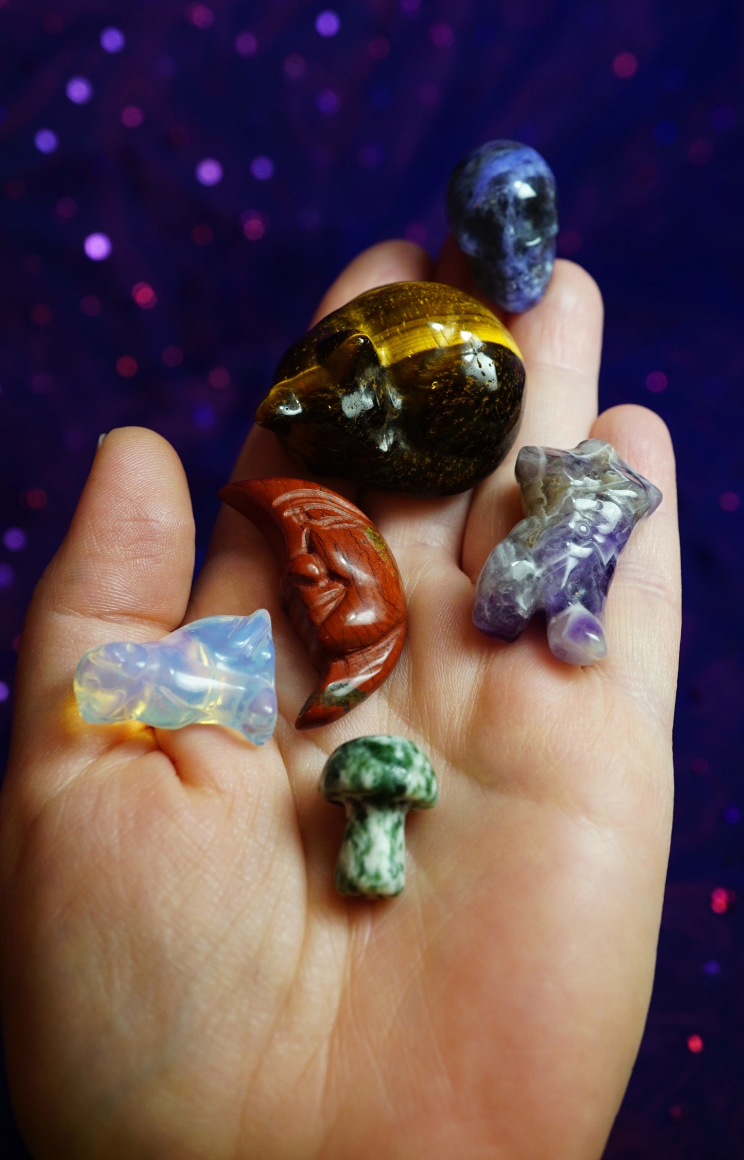 Hand holding various small crystals against a dark, starry background