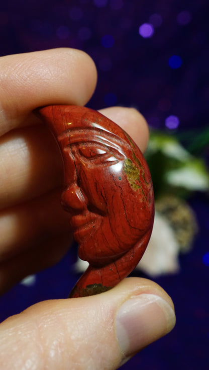 Hand holding a red stone with carvings against a blurred background