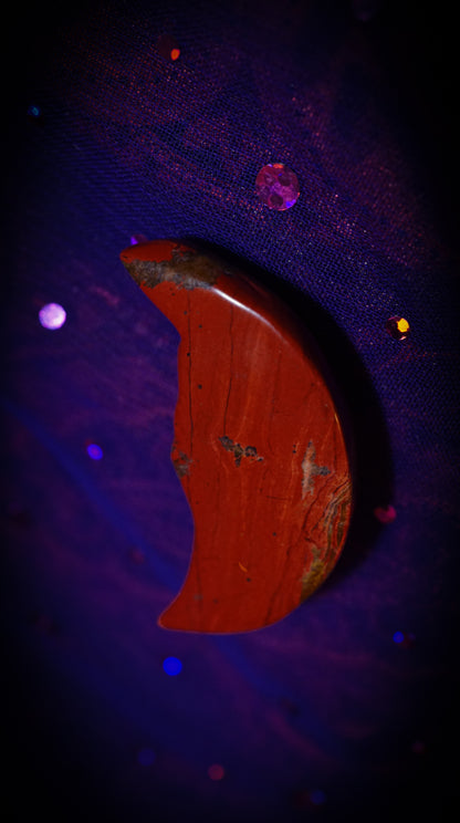 Red crescent moon stone on a dark background with glowing blue and purple lights