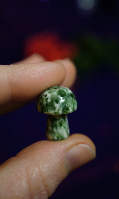 hand holding miniature green and white mushroom crystal against purple background