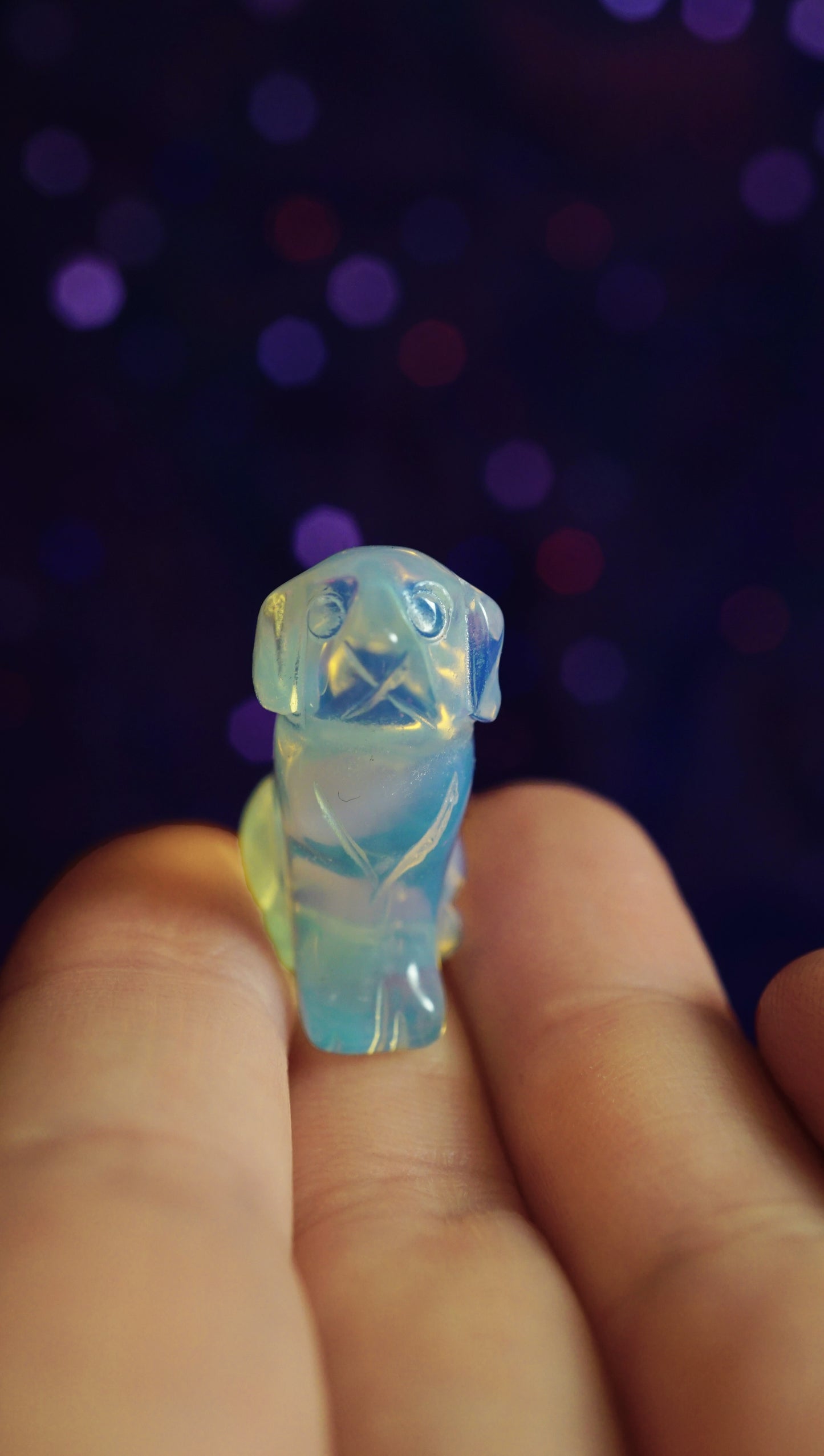 Opalite dog-shaped figure held between fingers against a dark, blurred background