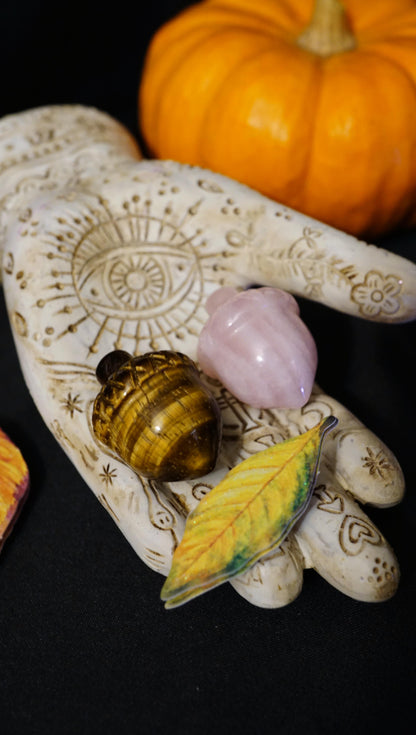 acorn stones in hamsa hand. dark background with orange pumpkin and yellow leaf. 