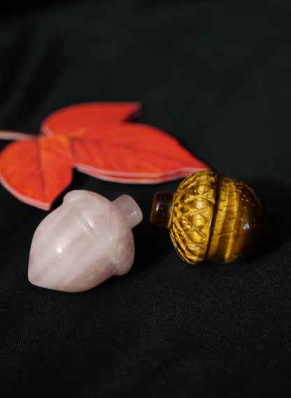 pink rose quartz acorn and tigers eye acorn carvings on black background, with red leaf