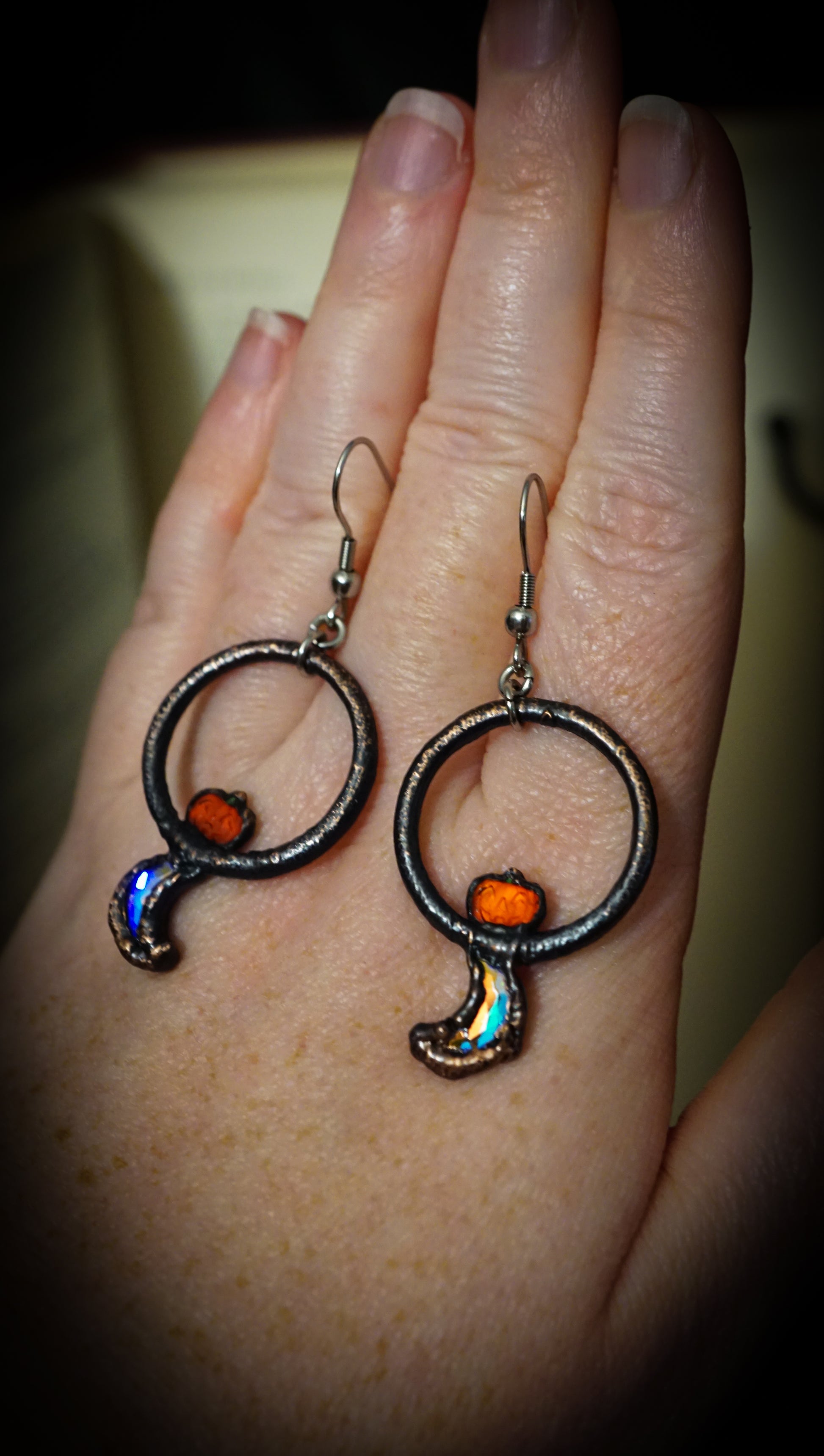 pair of dark copper hoops with flashy crescent moons and orange jack o lanter pumpkin rhinestones. on hand hanging from steel ear wires.