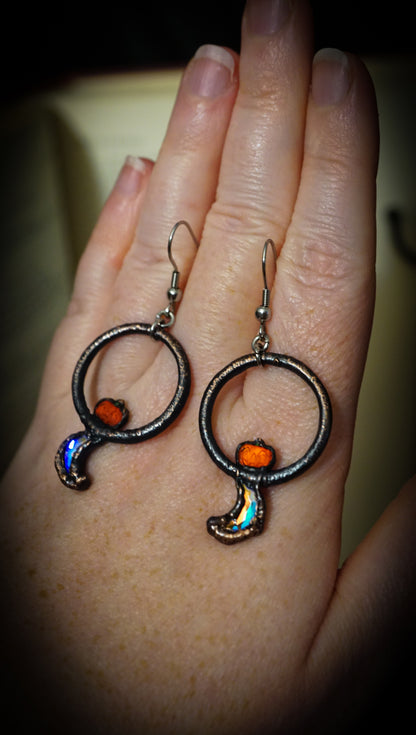 pair of dark copper hoops with flashy crescent moons and orange jack o lanter pumpkin rhinestones. on hand hanging from steel ear wires.