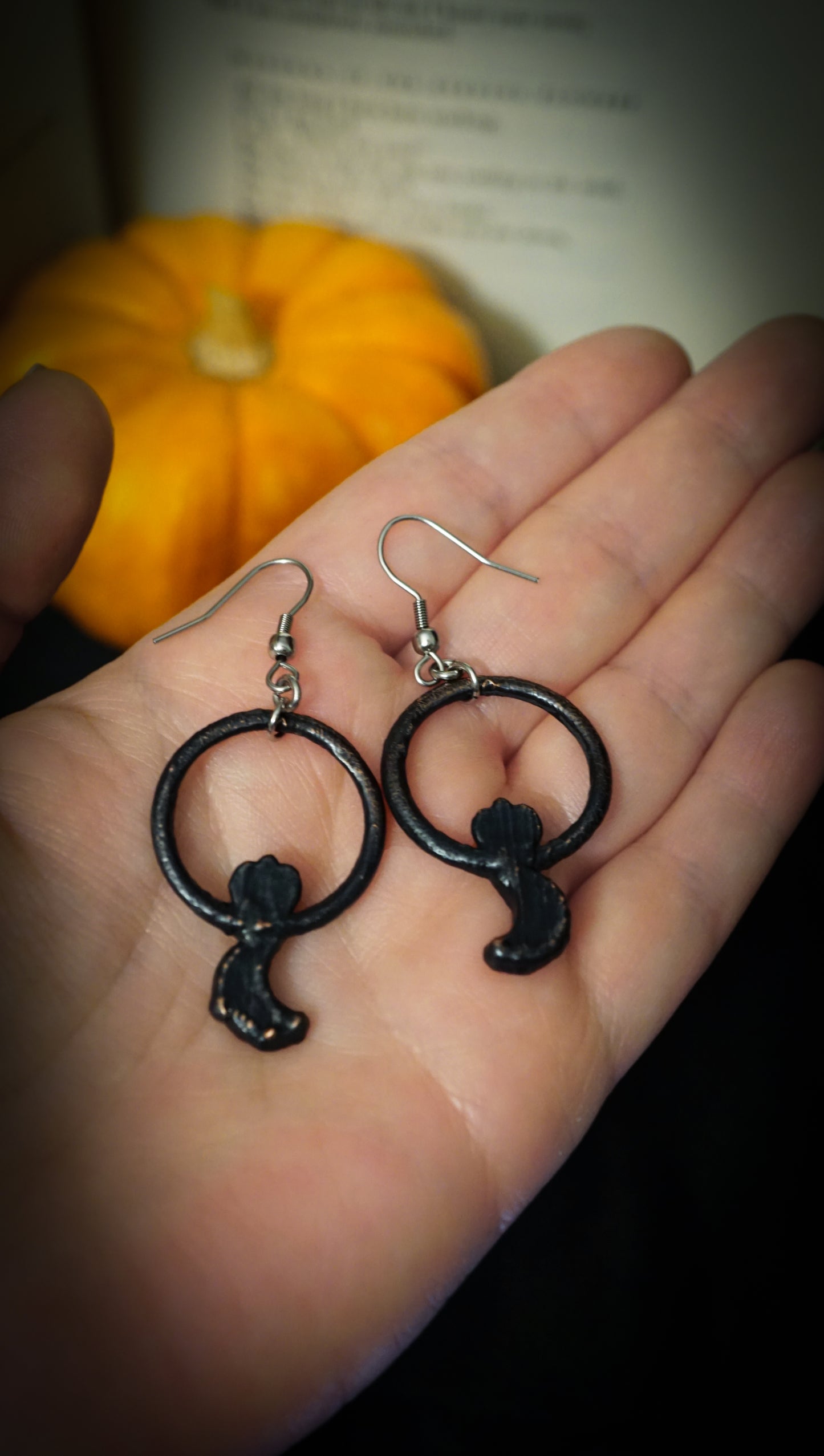 black copper backs of gothic hoop earrings, faced down on hand. small pumpkin and old book page in background.