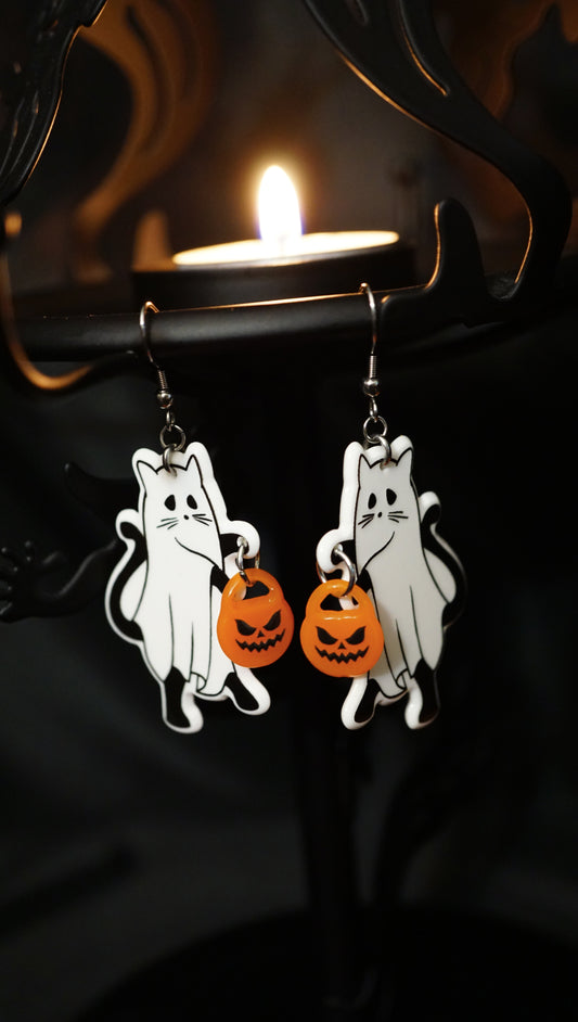 white ghost kitties holding orange pumpkin candy buckets--but they are earrings. hanging on a black candle holder with lit tealight candle