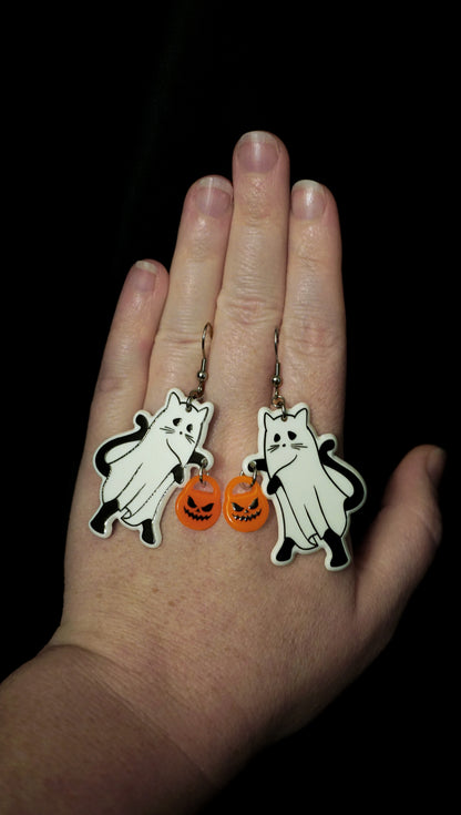 Hand holding Halloween-themed ghost earrings with black, white, and orange design on a dark background