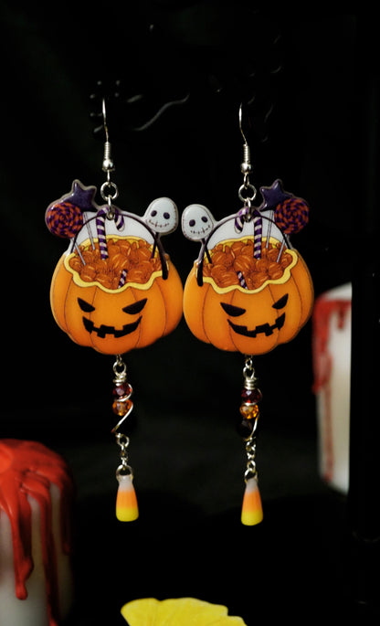 Halloween-themed pumpkin earrings with candy corn and skull decorations on a dark background.