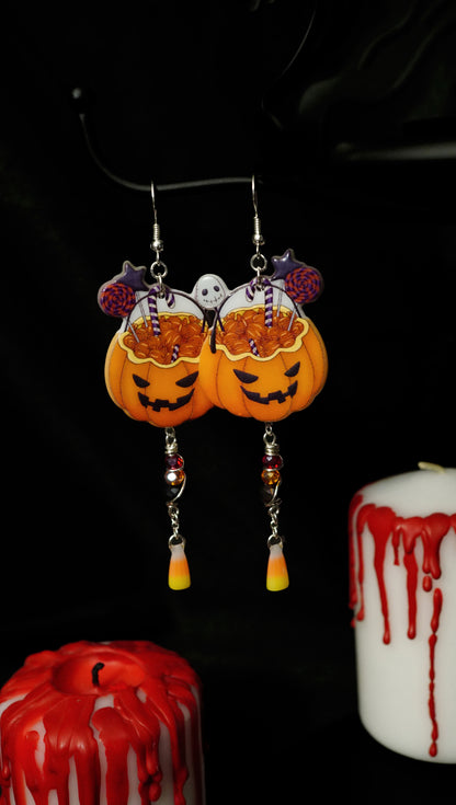 halloween earrings with orange jack o lantern candy buckets with dangling red, orange and black beads, and miniature fake candy corns. black background with white candles with red crayon dripped down the side. 