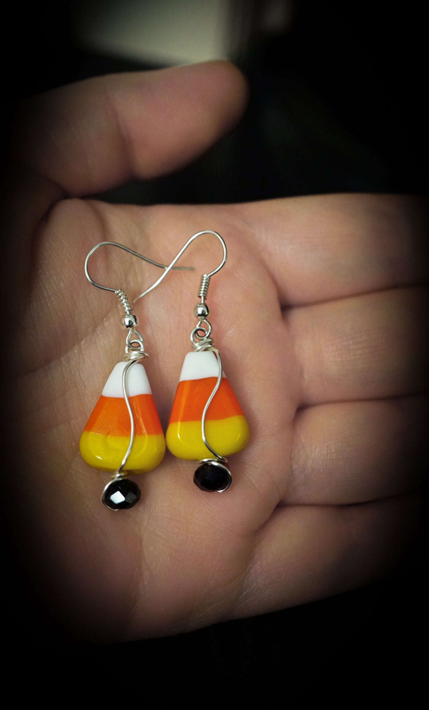 Candy corn-shaped earrings held in a hand against a dark background