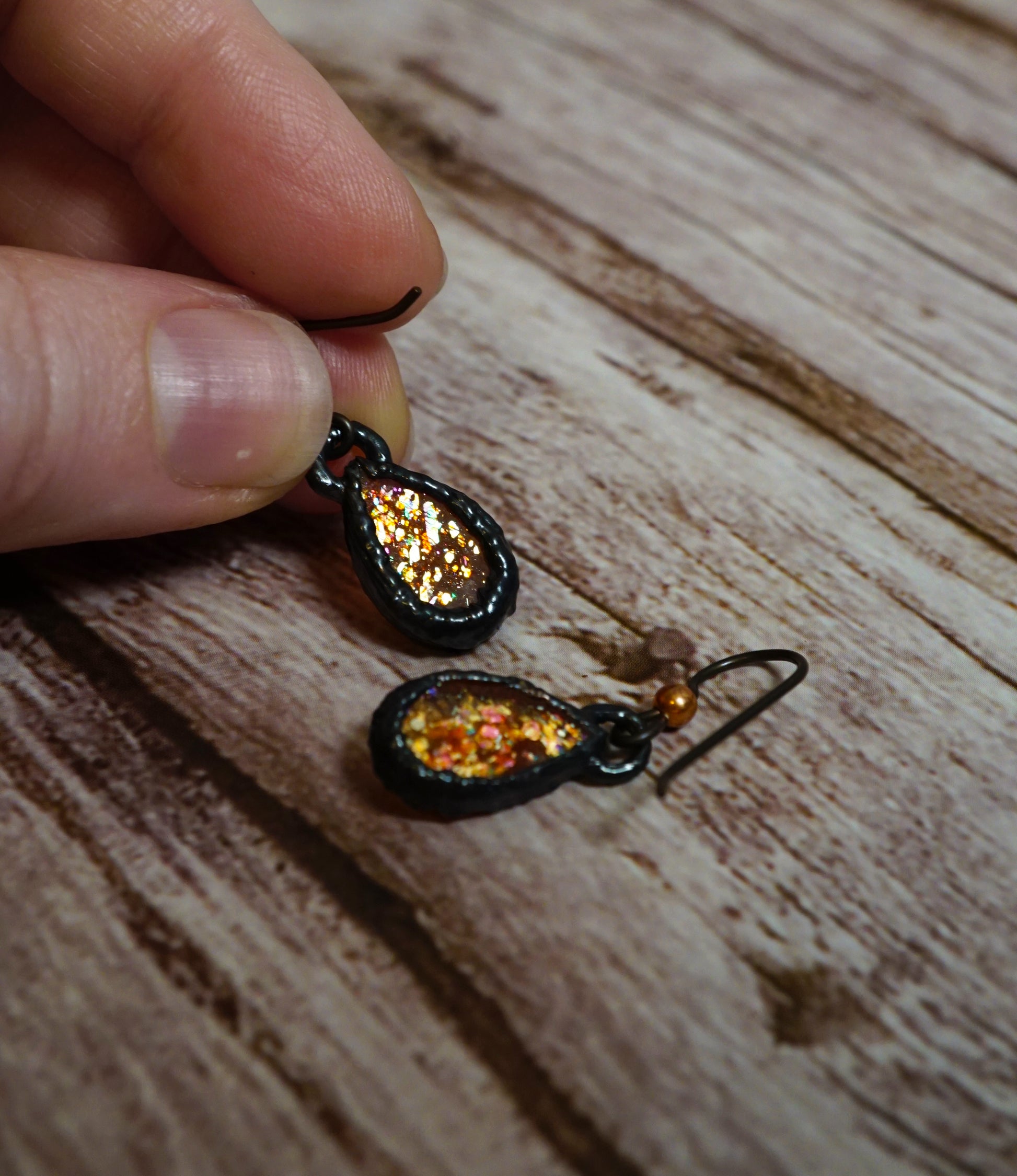 holding small orange and black earrings showing the backside sparkles, against wood background