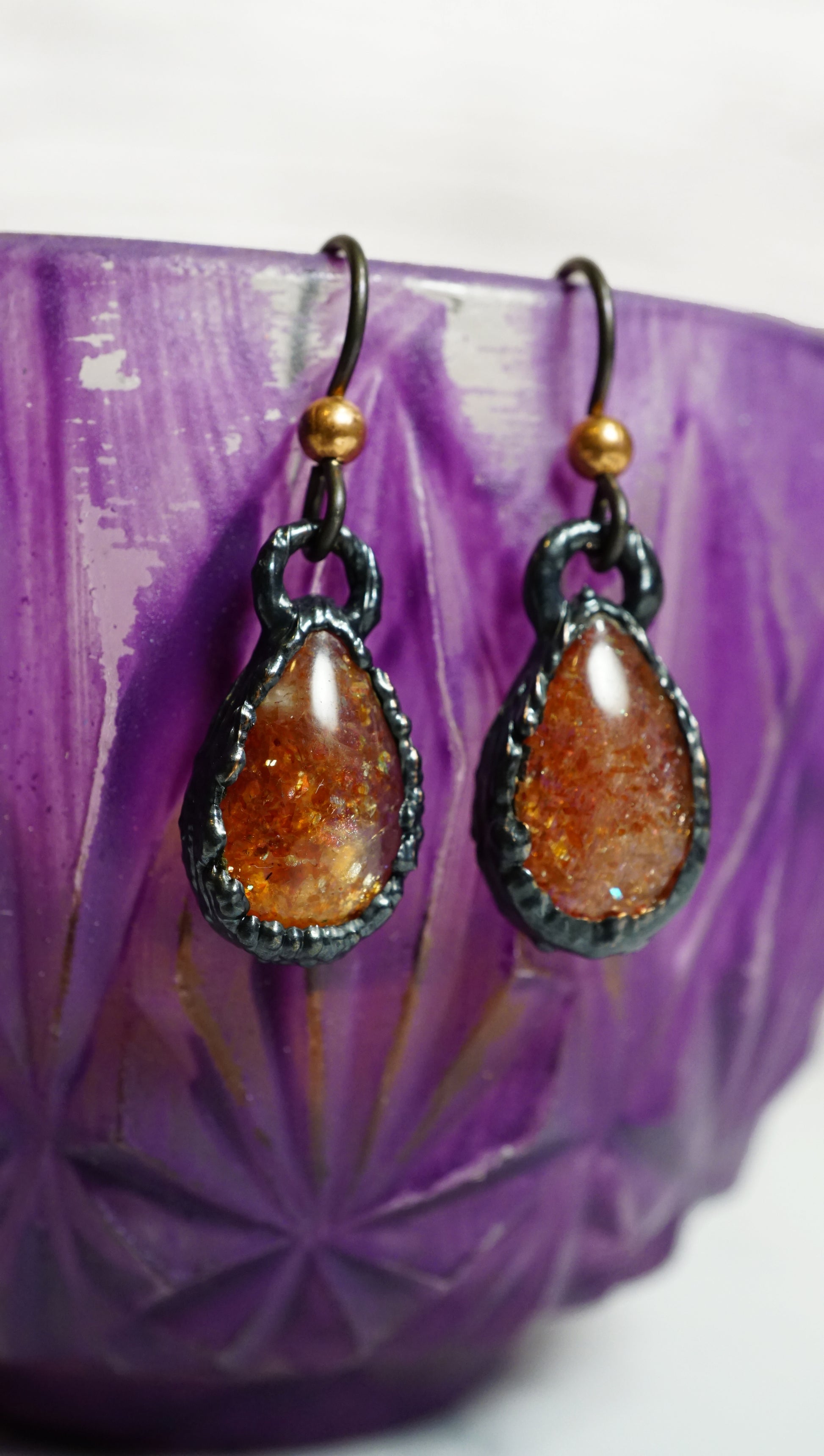 orange crystal earrings hanging on purple teacup. white background