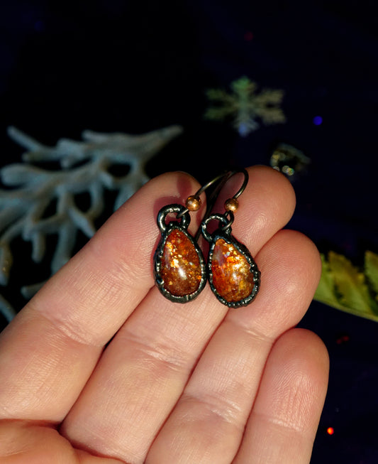 orange sunstone tear drop earrings with black copper on a hand, christmas blue and white background with snowflake