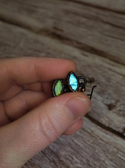 Hand holding a pair of glowing blue and green crystal earrings with a wooden surface background