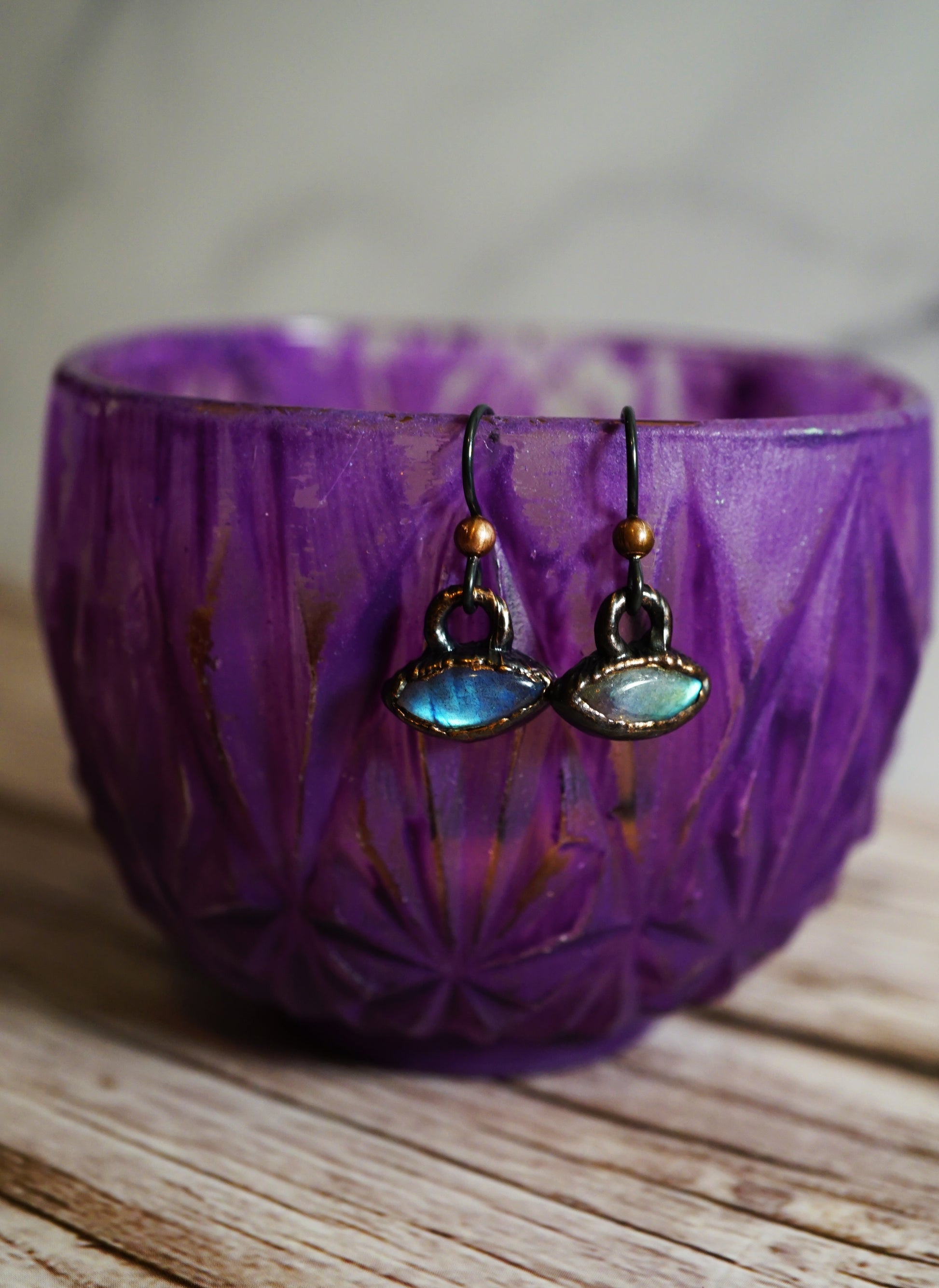 Pair of earrings with blue gemstones on a purple teacup 