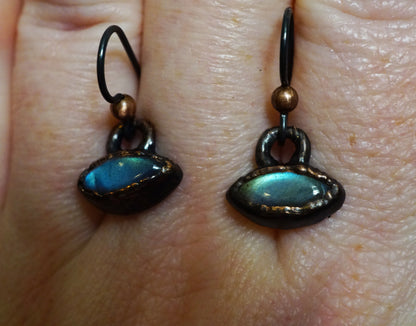 Pair of earrings with green and blue gemstones on a person's hand