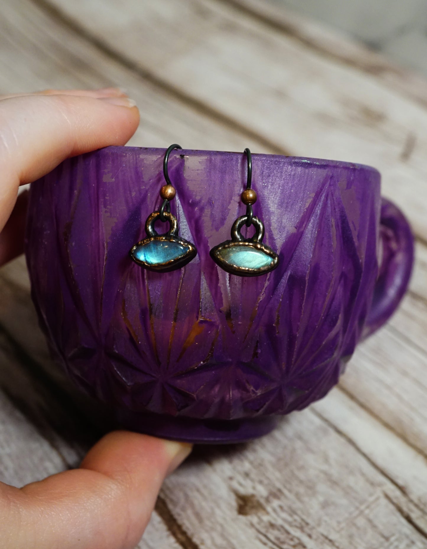 Purple cup with earrings hanging inside on a wooden surface