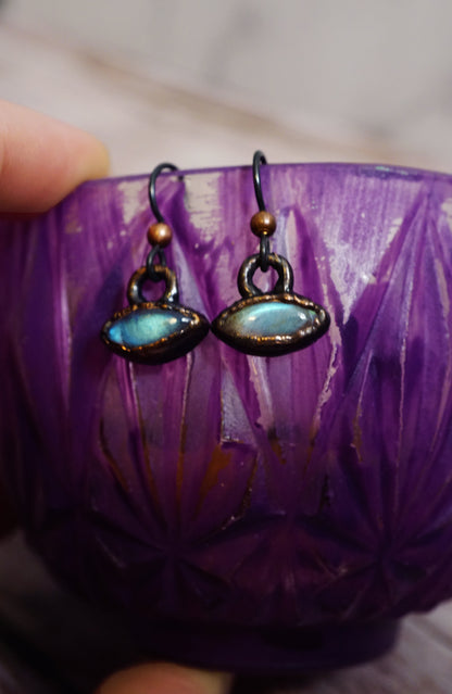 closeup of blue labradorite gemstone earrings, dainty settings. hanging on purple teacup