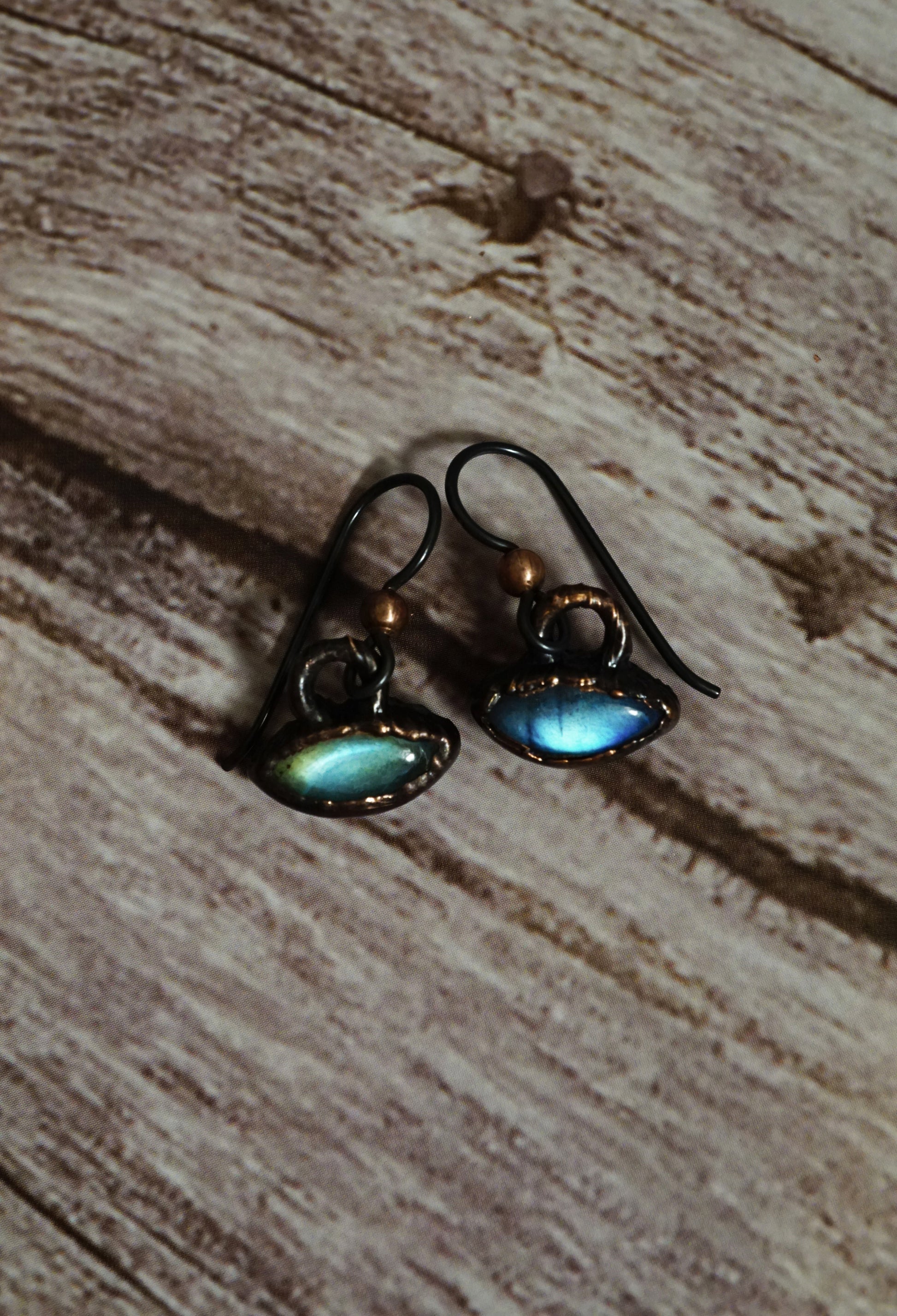 blue and green labradorite earrings that look like spaceship or eye shaped with dark copper settings. wooden background.