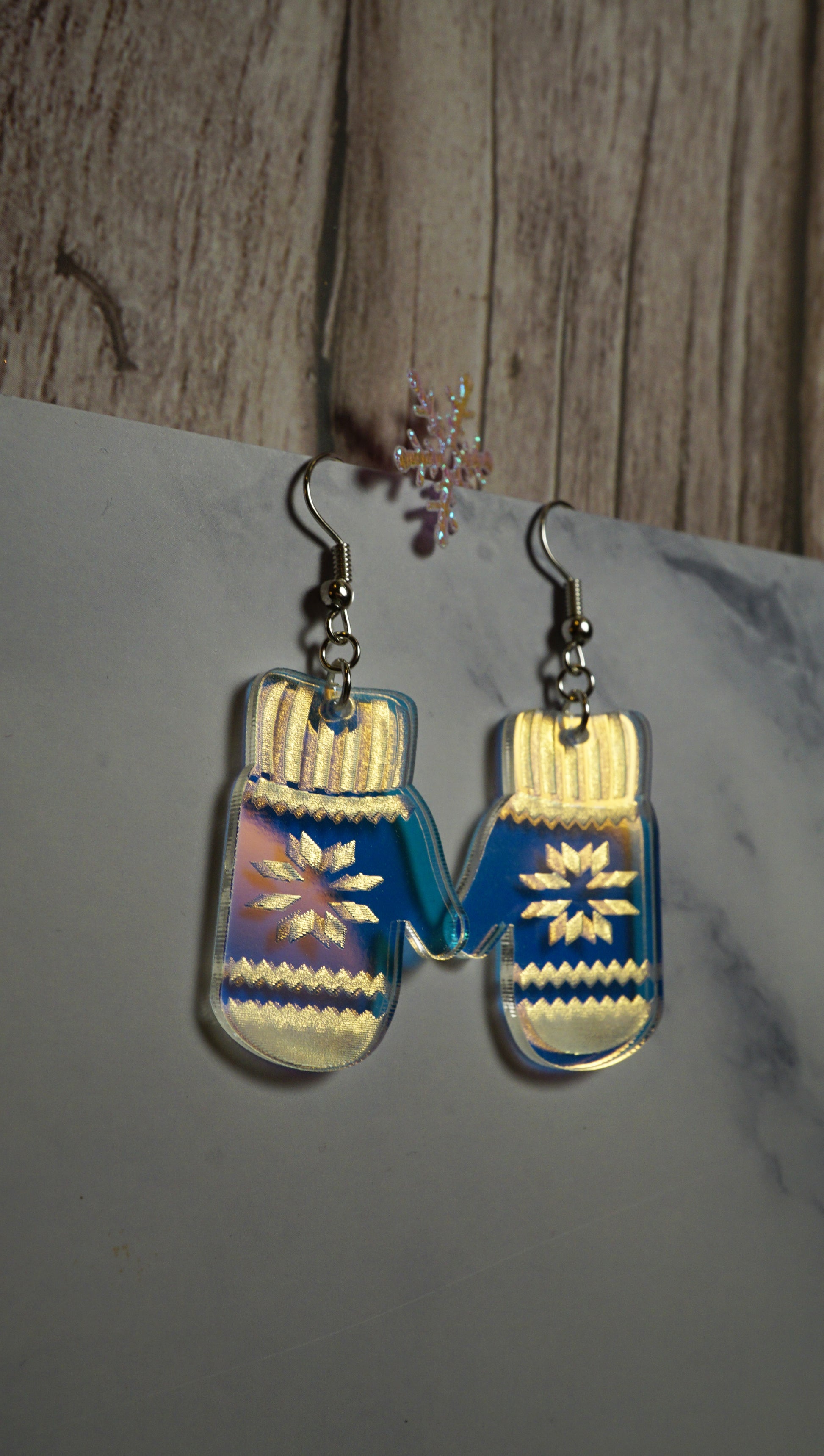 Mitten-shaped earrings with blue and gold design on a marble surface.