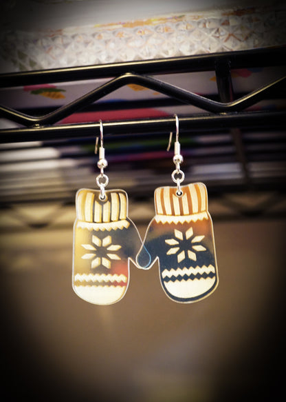Mitten-shaped earrings hanging on a stand with a blurred background