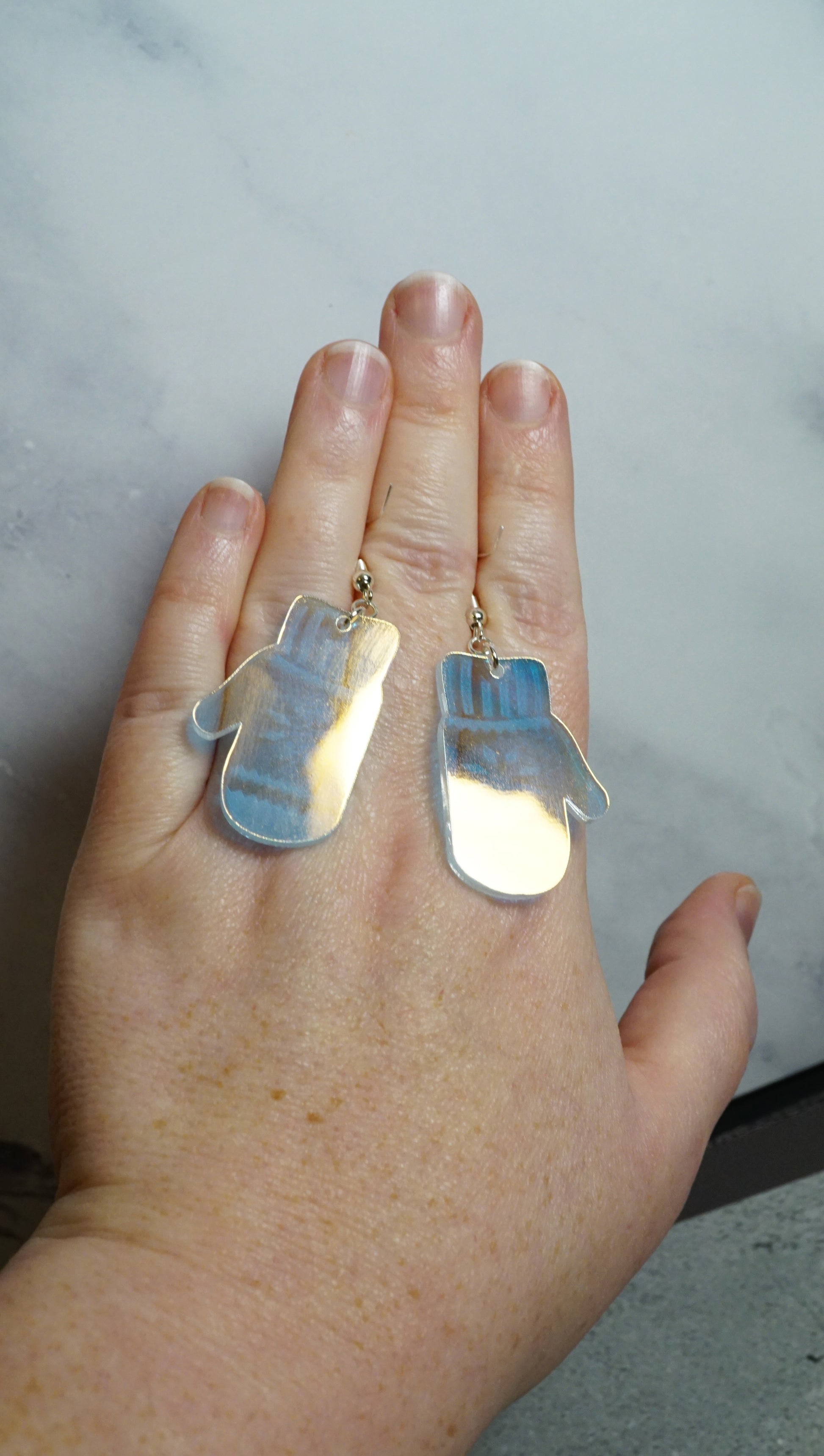 the shiny backside of iridescent mitten earrings on a hand