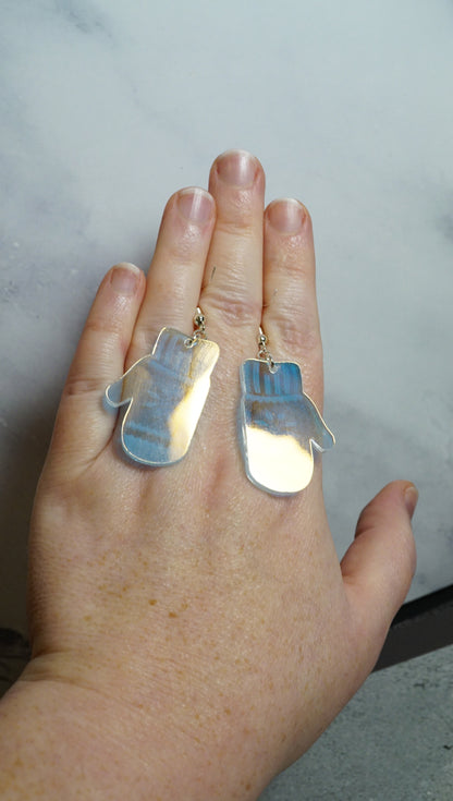 the shiny backside of iridescent mitten earrings on a hand