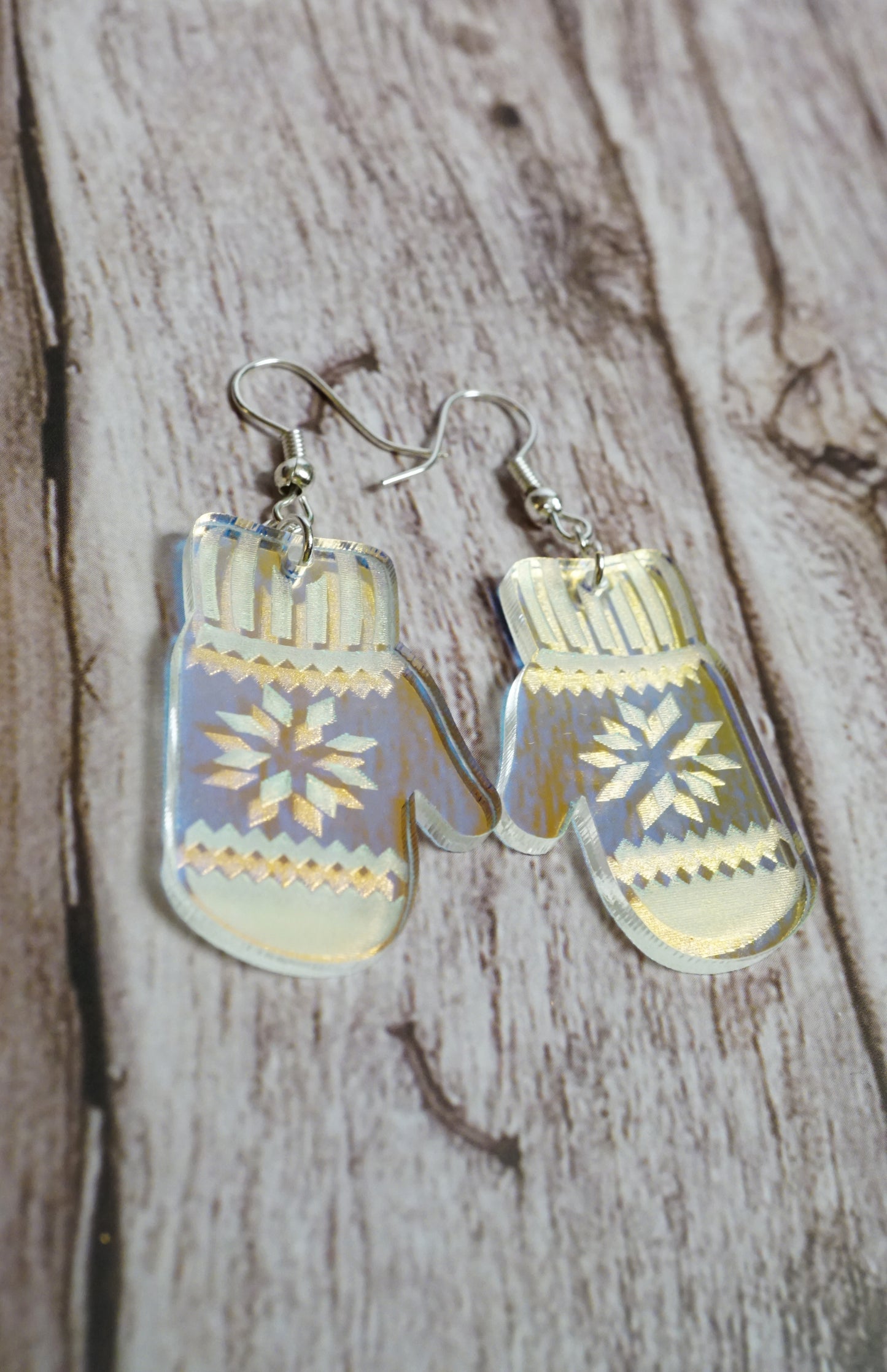 dangle earrings shaped like mittens with a snowflake pattern on a wooden surface.