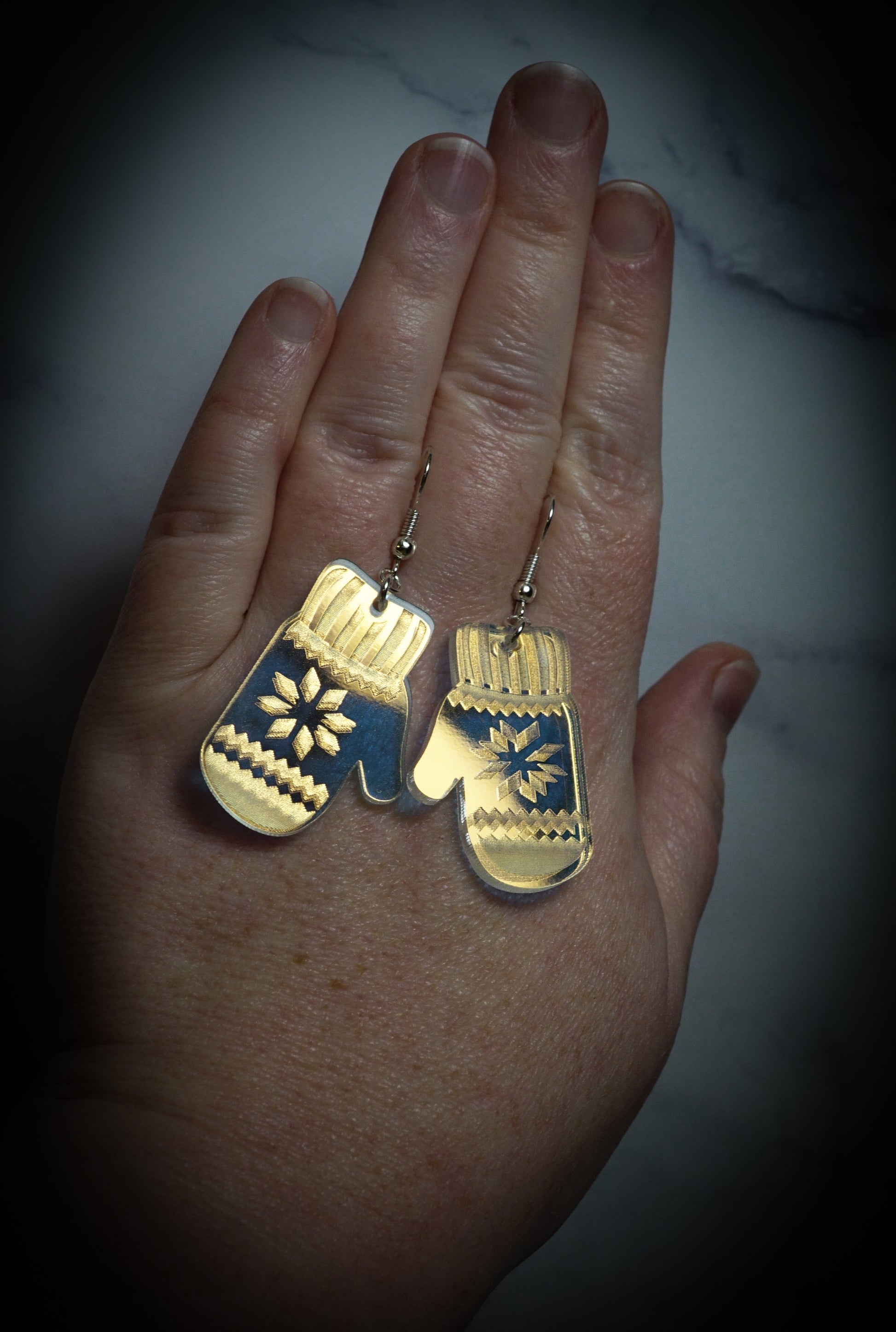 Gold mittens earrings held in a hand against a neutral background