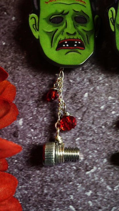 frankenstein monster face earring with red blood drop beads. grey background