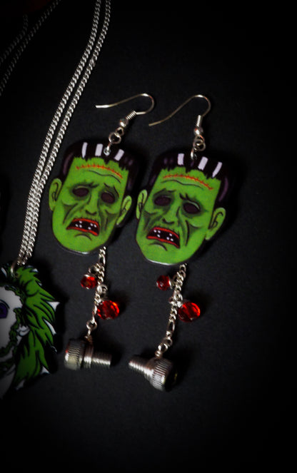 Green monster face earrings with red gemstones on a dark background