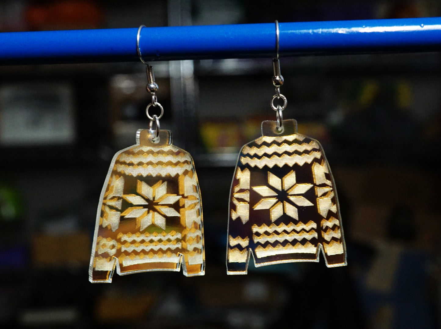 Sweater-shaped earrings on a blue rod with a blurred background