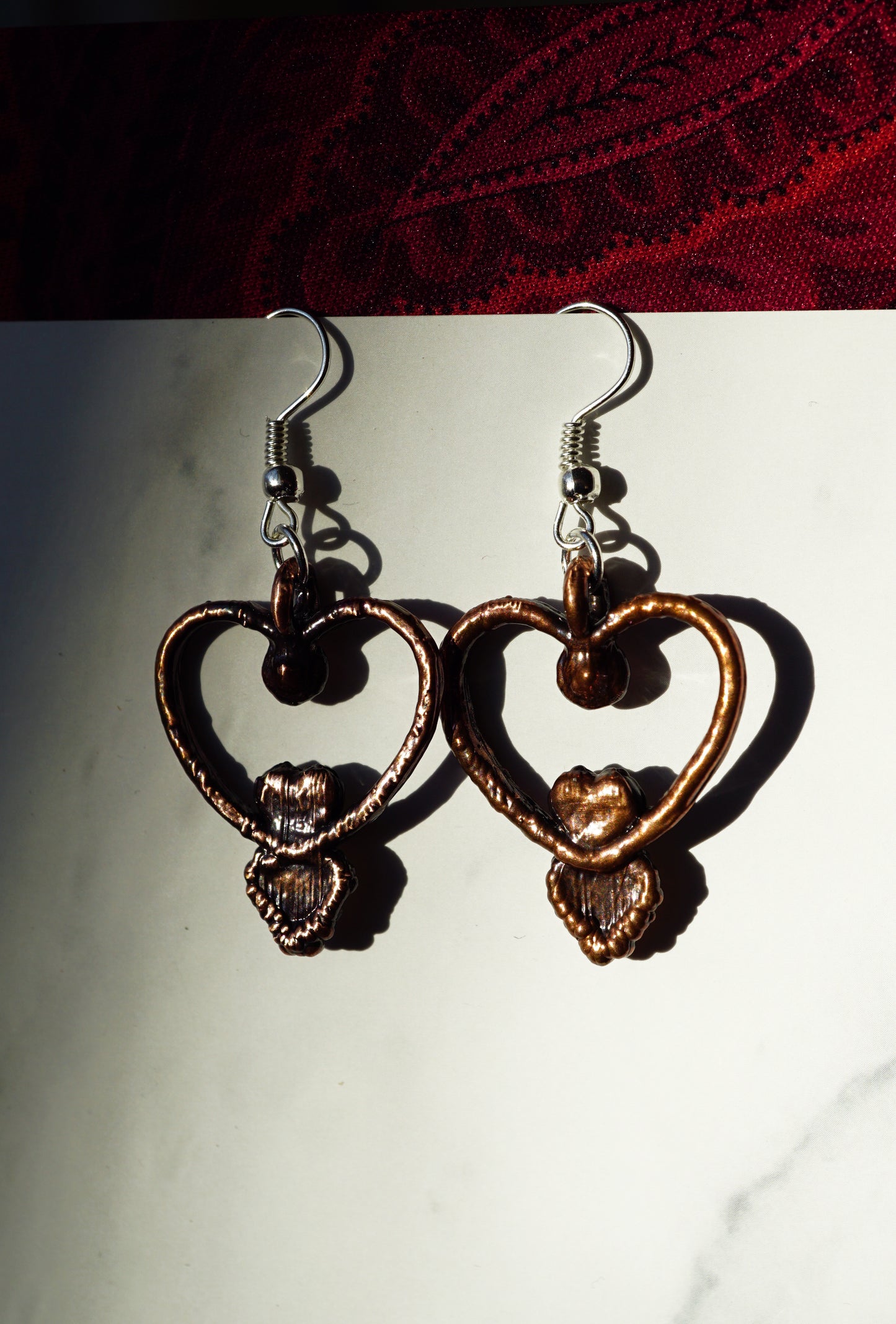 heart earrings, showing the copper backside. against white paper on a red fabric background