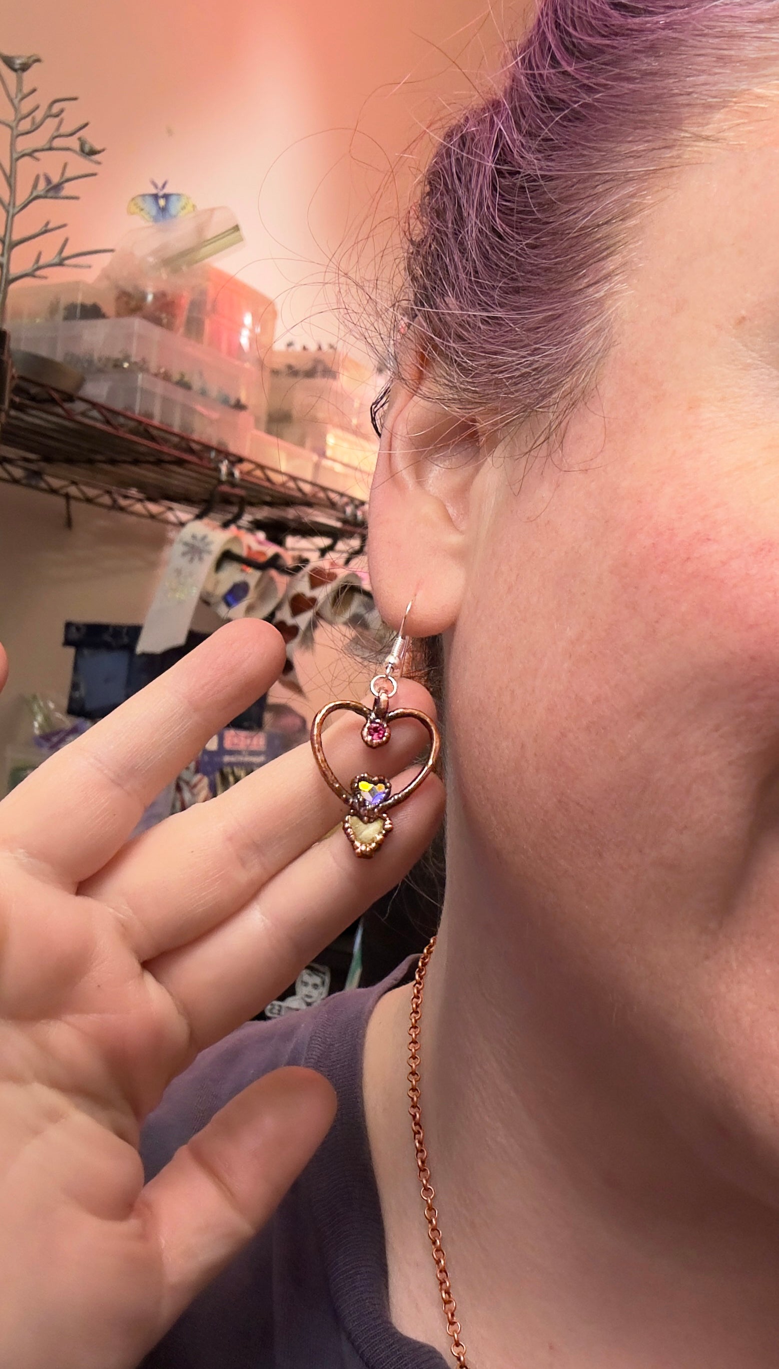 Close-up of a person wearing a heart-shaped earring with a colorful center.