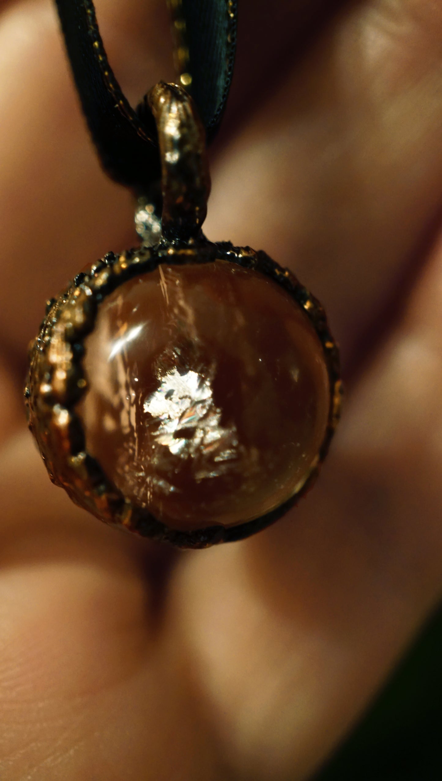 close up of clear quartz pendant with copper setting and black ribbon. in hand
