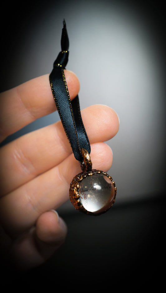 hand holding small quartz sphere ornament with black ribbon. grey background