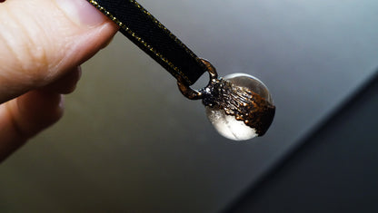side view of  textured copper on clear quartz ornament with black ribbon and grey background. 