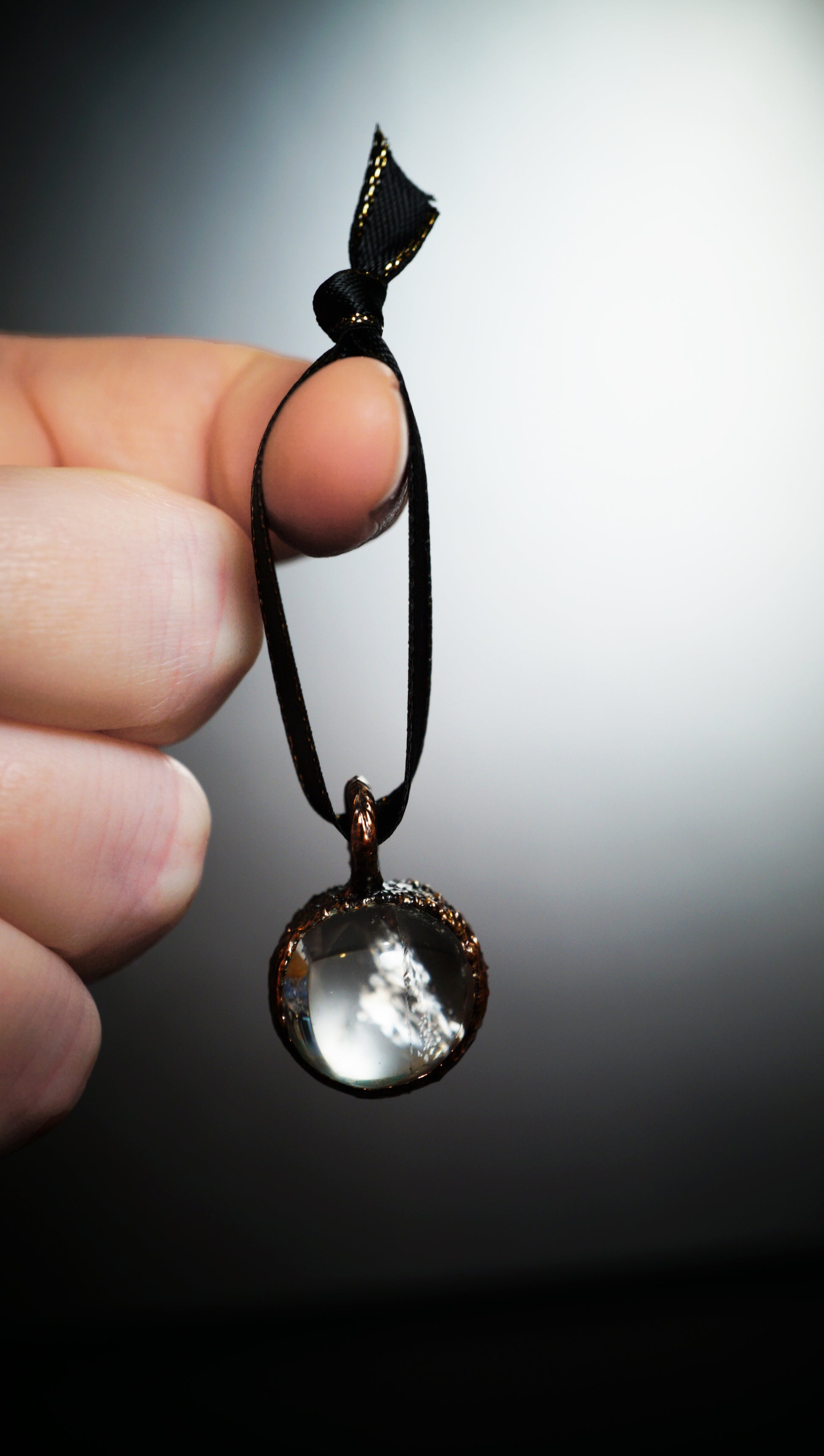 hand holding hanging ornament with clear stone, grey background